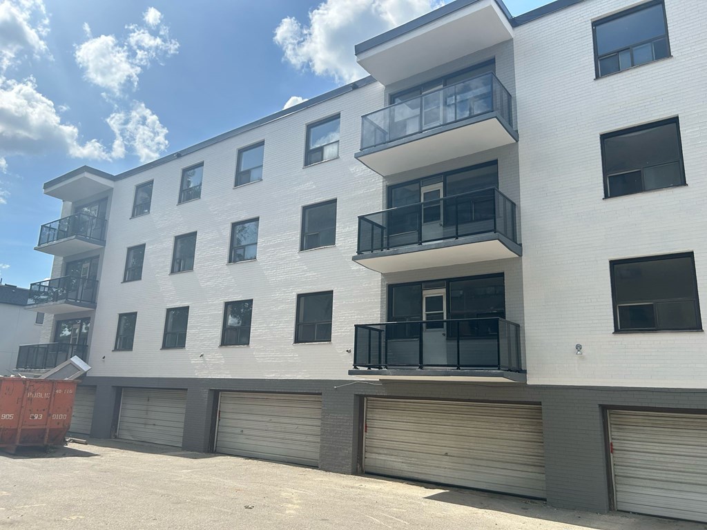 A white apartment building with black railings and closed grey garage doors.