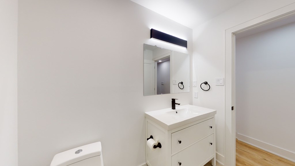 A white bathroom with a sink, mirror, and toilet.