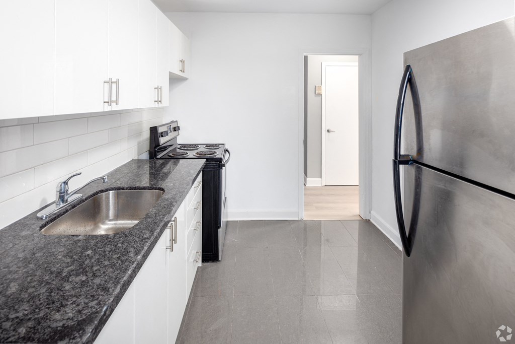 A kitchen with a black granite countertop and a stainless steel refrigerator.