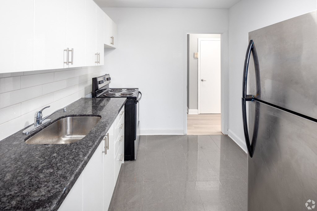 A modern kitchen with a stainless steel refrigerator and black granite countertops.