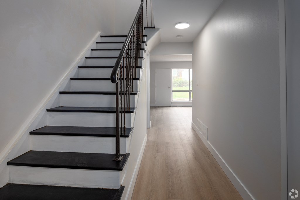 A long hallway with a staircase on the left and a door on the right.