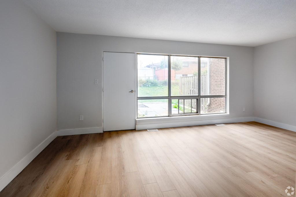 A room with a white door and a window with a view of a fence and houses.