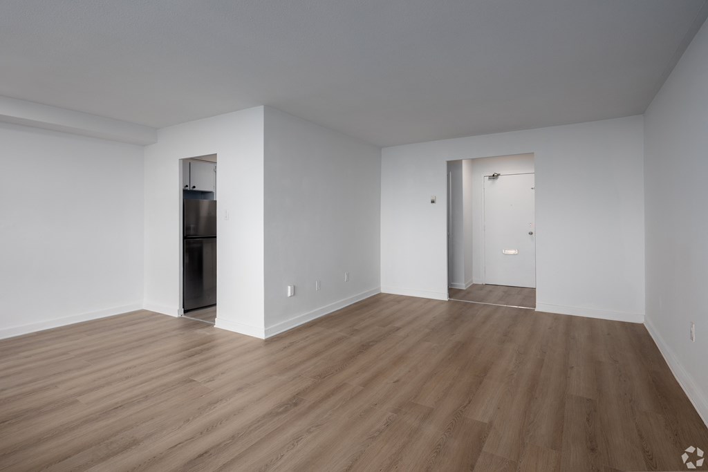 A room with wooden floors and white walls, with a door on the left and a window on the right.