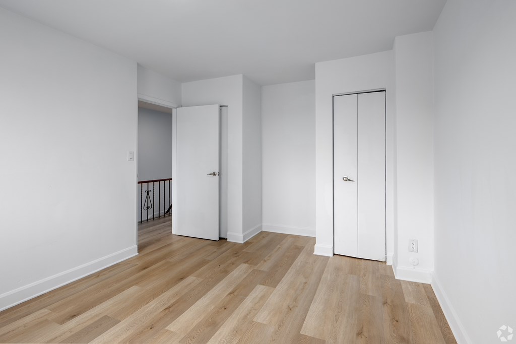 A room with white walls and wooden flooring with two white doors.