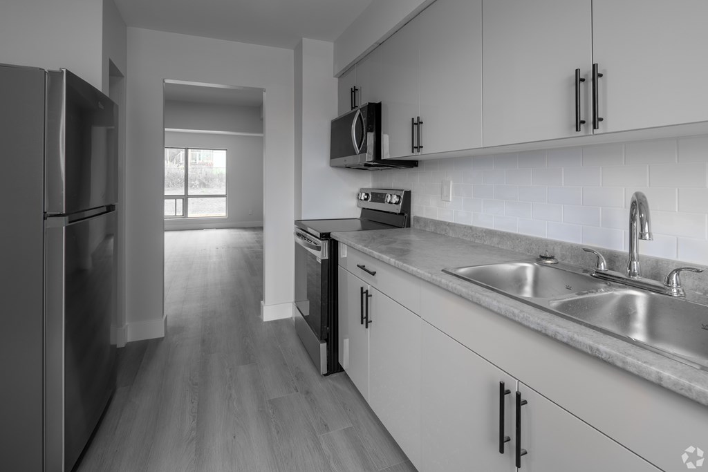 A kitchen with a refrigerator, microwave, oven, and sink.