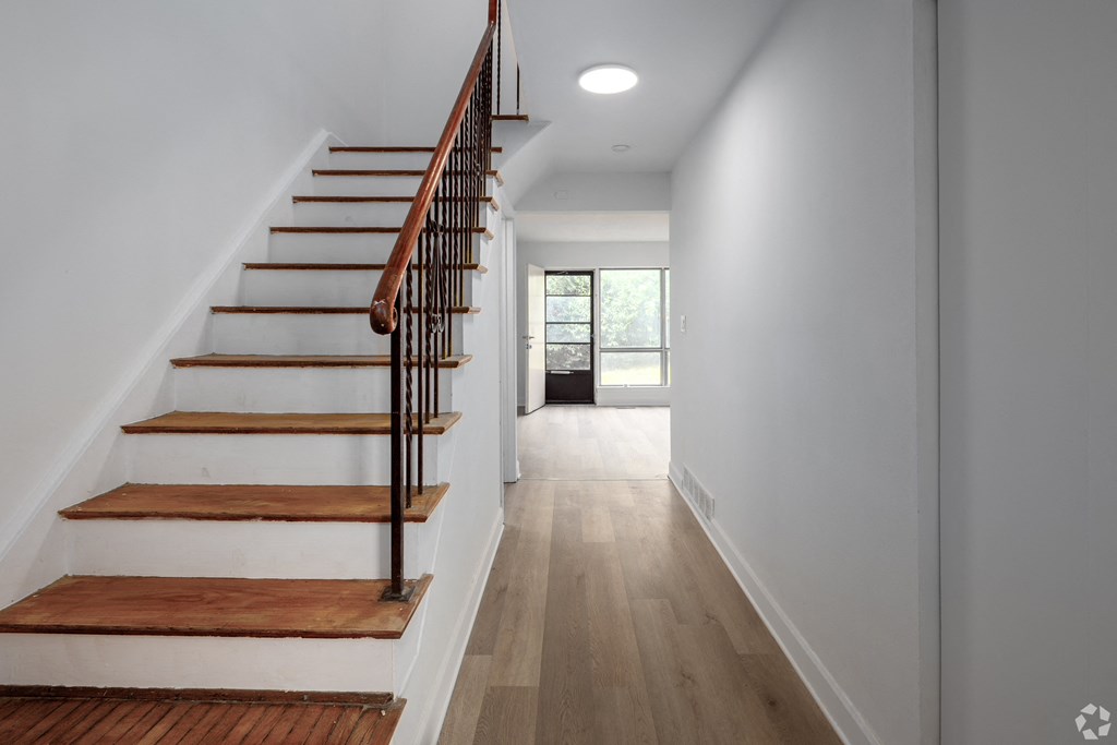 A long hallway with a staircase on the left and a door on the right.