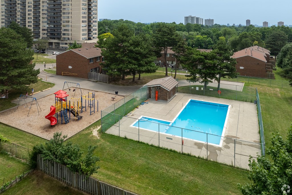 A playground with a slide, swings, and a basketball court is surrounded by a fence and a pool.
