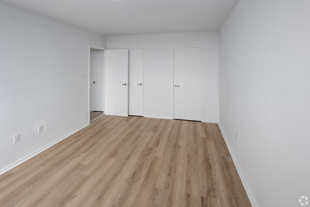 A room with white walls and wooden flooring with three white doors.