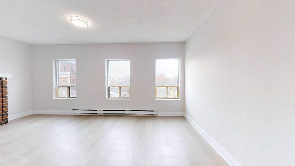 A large empty room with a bench and three windows.