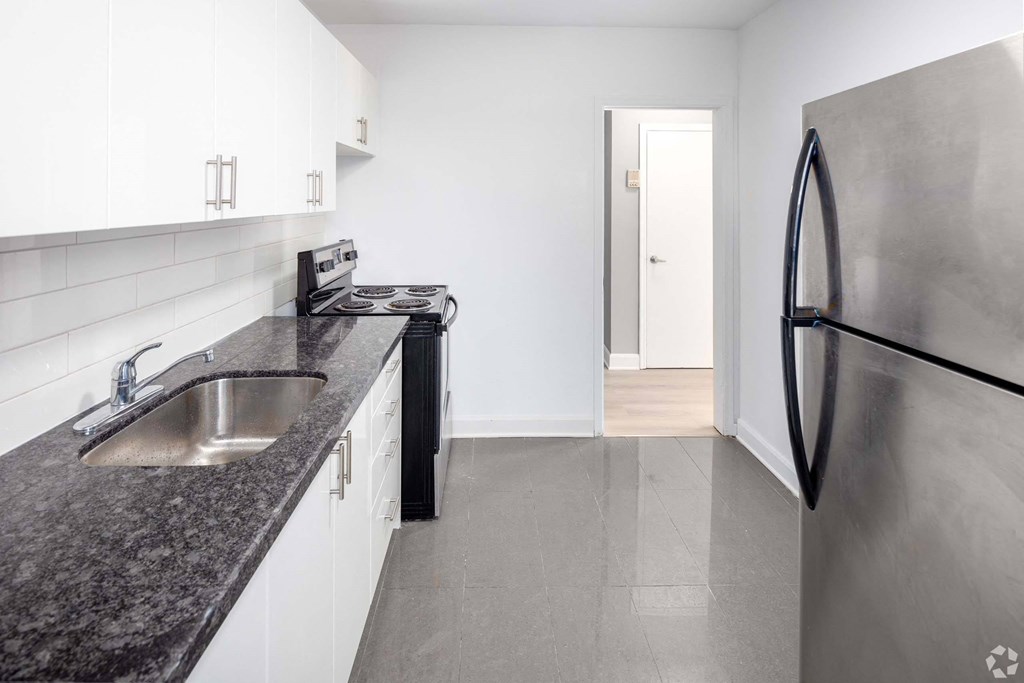 A kitchen with a black granite countertop and a stainless steel refrigerator.