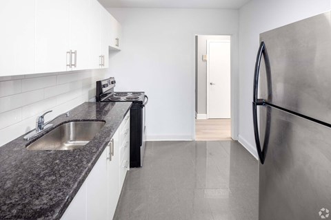 A kitchen with a black granite countertop and a stainless steel refrigerator.