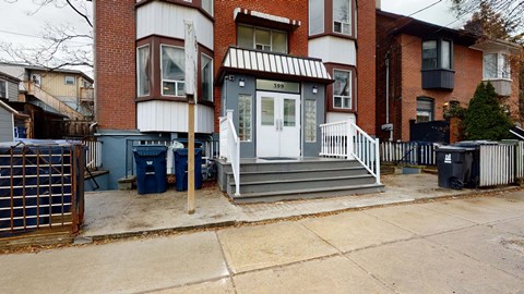A house with a white door and a black trash can in front of it.