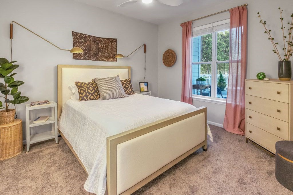 A bedroom with a large bed, a nightstand, and a window with pink curtains.
