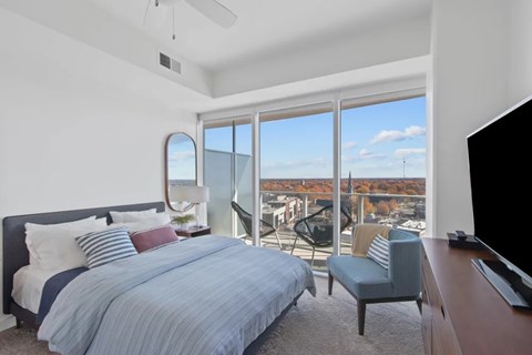 A bedroom with a large bed and a balcony overlooking a cityscape.