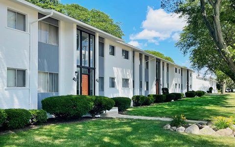 A row of white apartment buildings with green bushes in front.