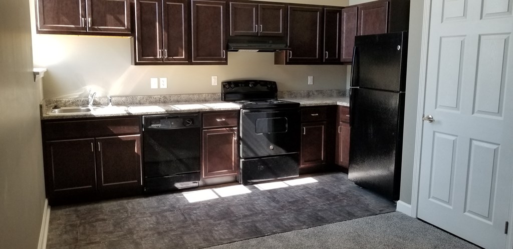 an empty kitchen with black appliances and dark wood cabinets