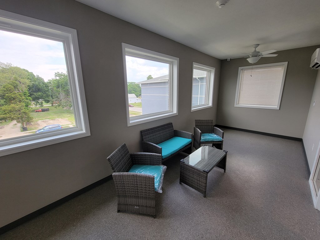 a living room with wicker chairs and a table and three windows