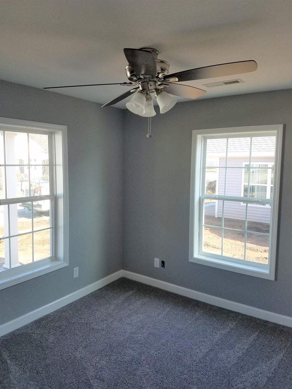 an empty room with a ceiling fan and two windows