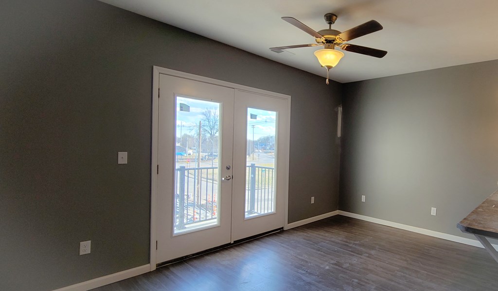 an empty living room with a ceiling fan and doors to a balcony