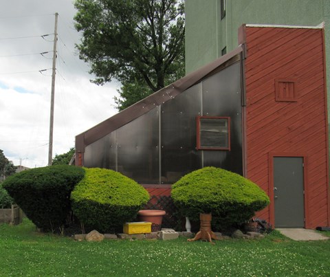 the side of a house with a greenhouse and some bushes