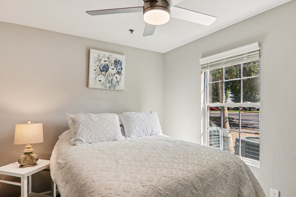 A bedroom with a bed, a lamp, and a ceiling fan.