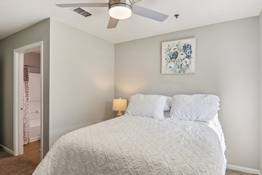 A bedroom with a bed, a ceiling fan, and a painting on the wall.