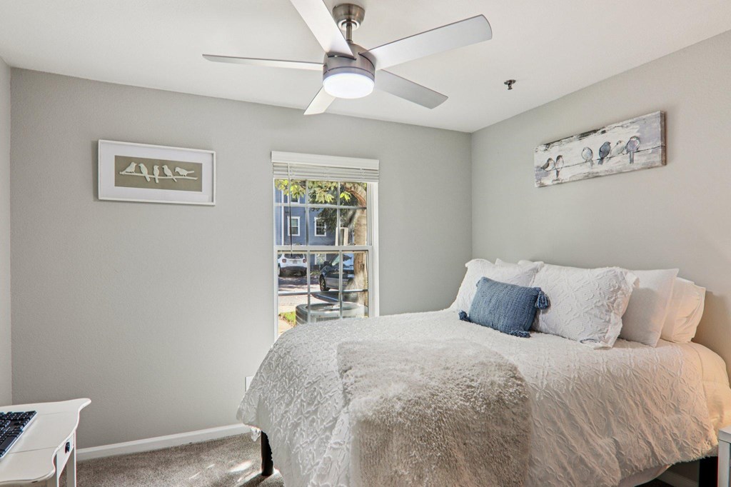 A bedroom with a bed, a ceiling fan, and two pictures on the wall.