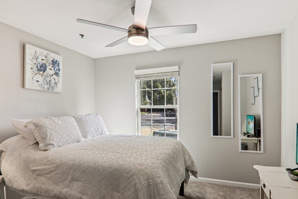 A bedroom with a bed, dresser, mirror, and a ceiling fan.