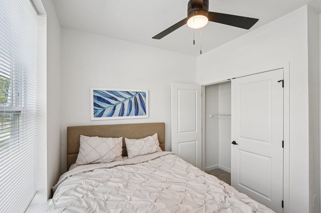A bedroom with a bed, a ceiling fan, and a painting on the wall.