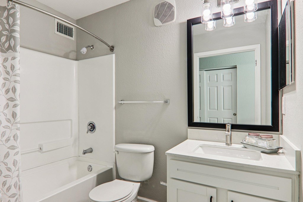 A white bathroom with a toilet, sink, and mirror.