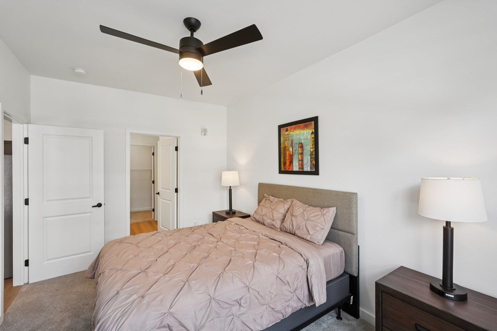 A bedroom with a bed, nightstand, and a ceiling fan.