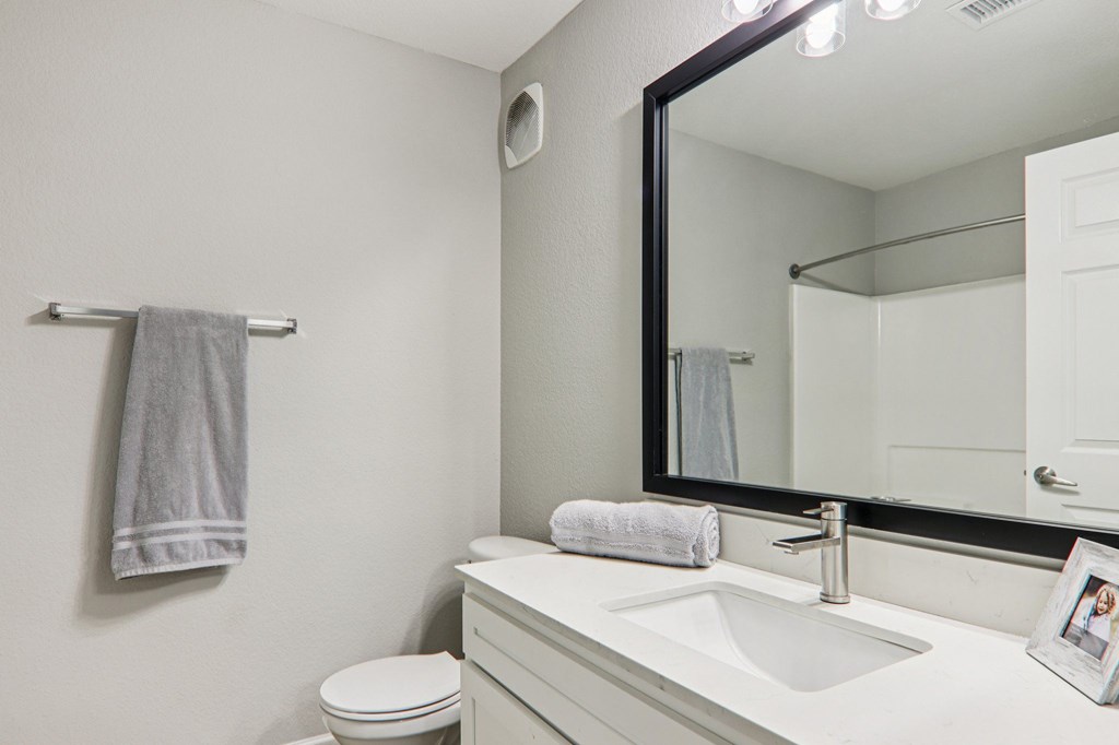 A bathroom with a toilet, sink, mirror, and towel rack.