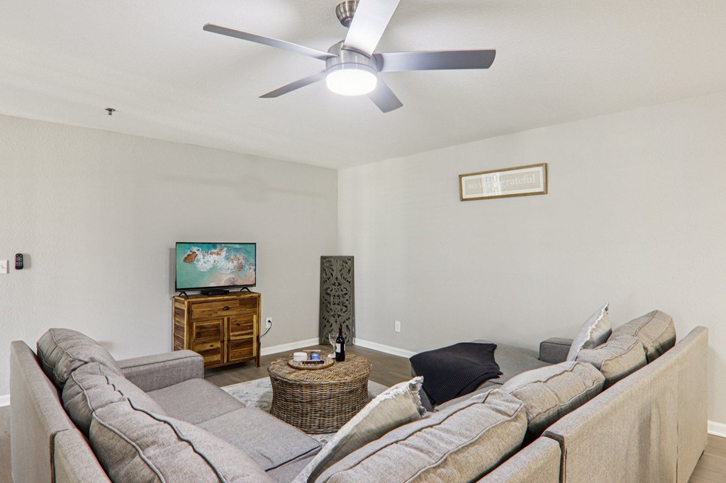 A living room with a grey couch and a ceiling fan.