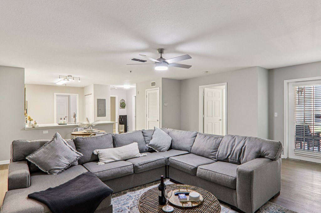 A grey sectional sofa with a black throw pillow sits in a living room with a ceiling fan and a coffee table.