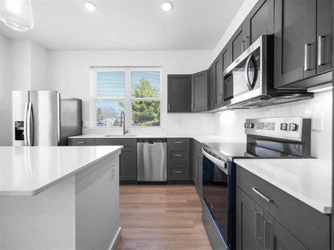 A modern kitchen with dark cabinets and stainless steel appliances.