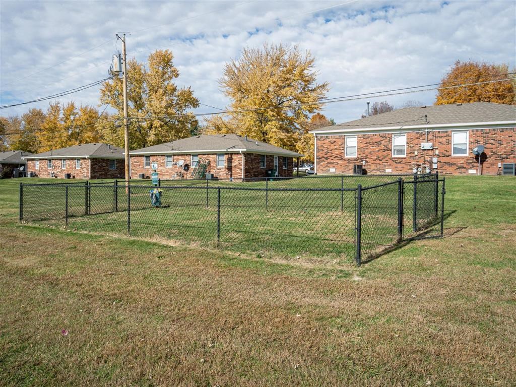 A person is standing in a grassy field next to a fence.