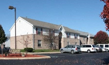A white building with a grey roof and a parking lot in front.