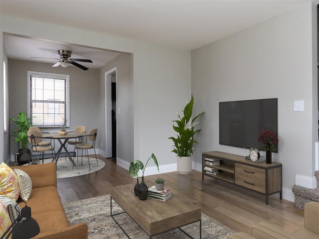 A living room with a brown couch, a coffee table, a dining table with chairs, a flat screen TV, and a ceiling fan at Huntley Ridge Apartments, Kettering