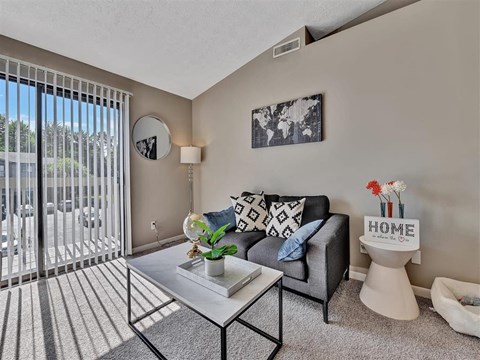 A living room with a grey couch, a coffee table, and a sign that says "HOME".