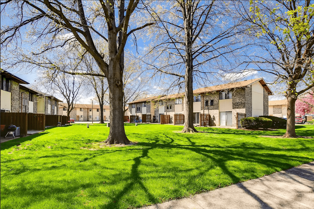 A grassy area with trees and apartment buildings in the background.