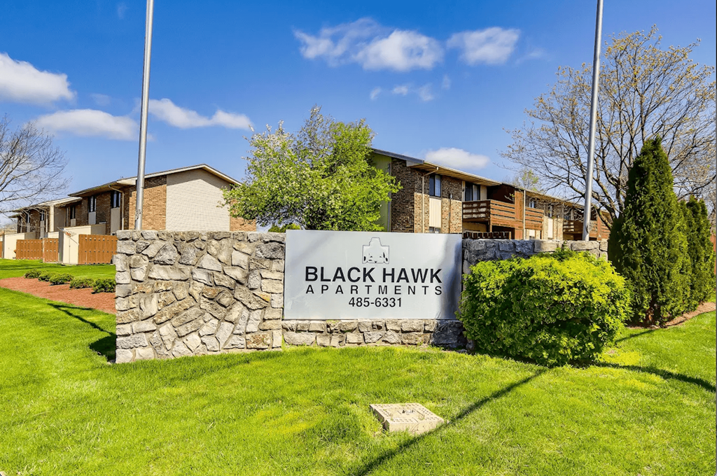 A sign for Black Hawk Apartments stands in front of a building.