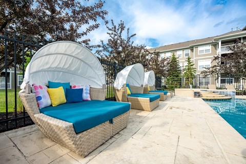A poolside lounge area with white wicker chairs and cushions.