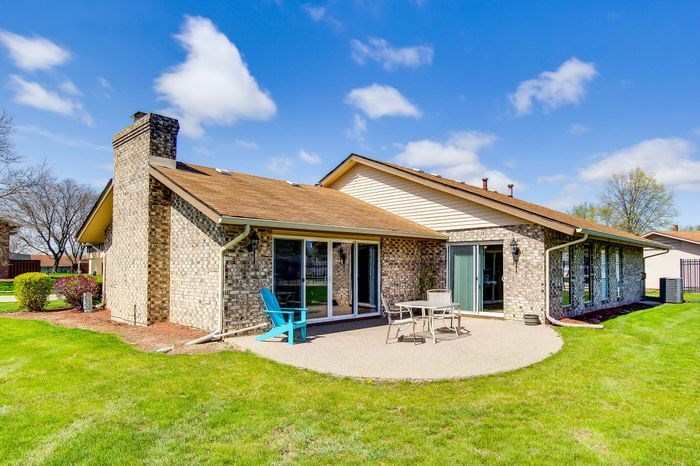 A house with a stone chimney and a blue chair on the patio.