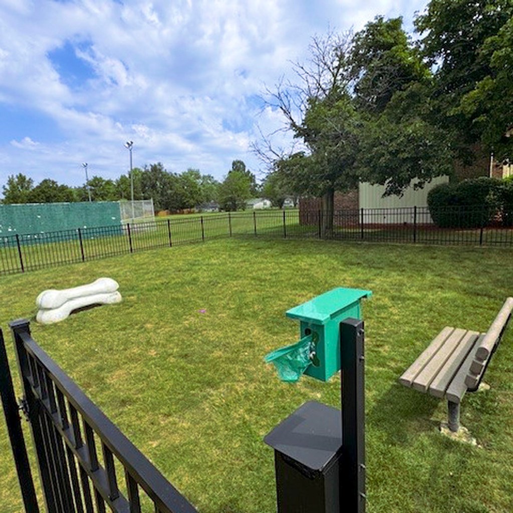 A dog park with a green trash can and a bench.