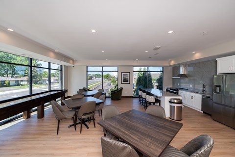 A modern community room kitchen with a dining table, comfortable chairs and shuffle board game.