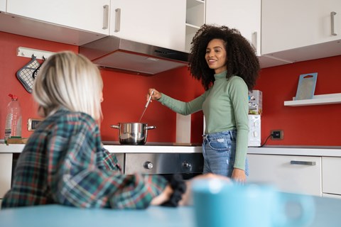 A woman with curly hair is standing in a kitchen and holding a spoon.