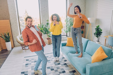 Three people are dancing in a bright room with a blue couch and a white wall.