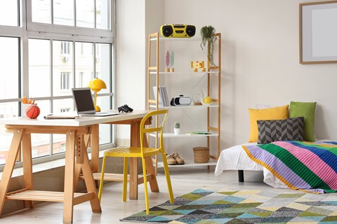 A room with a desk, chair, and a bed with a colorful blanket.