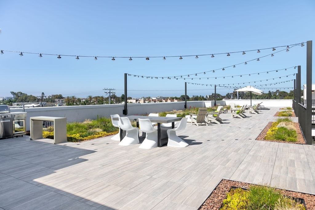 A patio with white chairs and tables is decorated with string lights.
