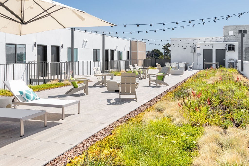A patio with chairs and umbrellas is surrounded by a grassy area.